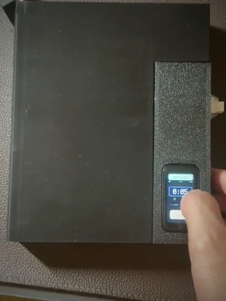 The same box with a finger on the touchscreen, setting a timer that reads 0:05, with the lock button below it.